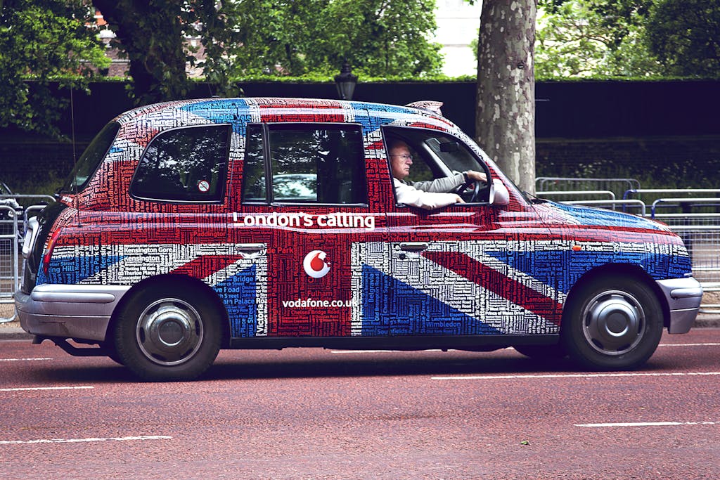 A vibrant Union Jack styled London taxi driving through central London.