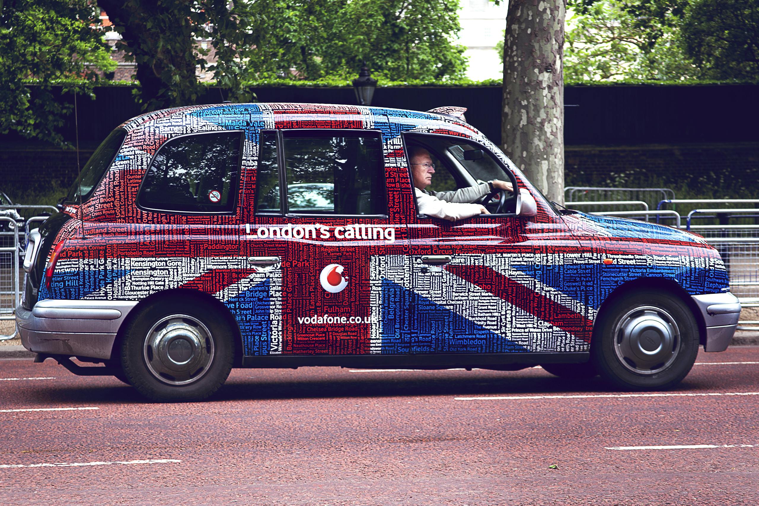 A vibrant Union Jack styled London taxi driving through central London.