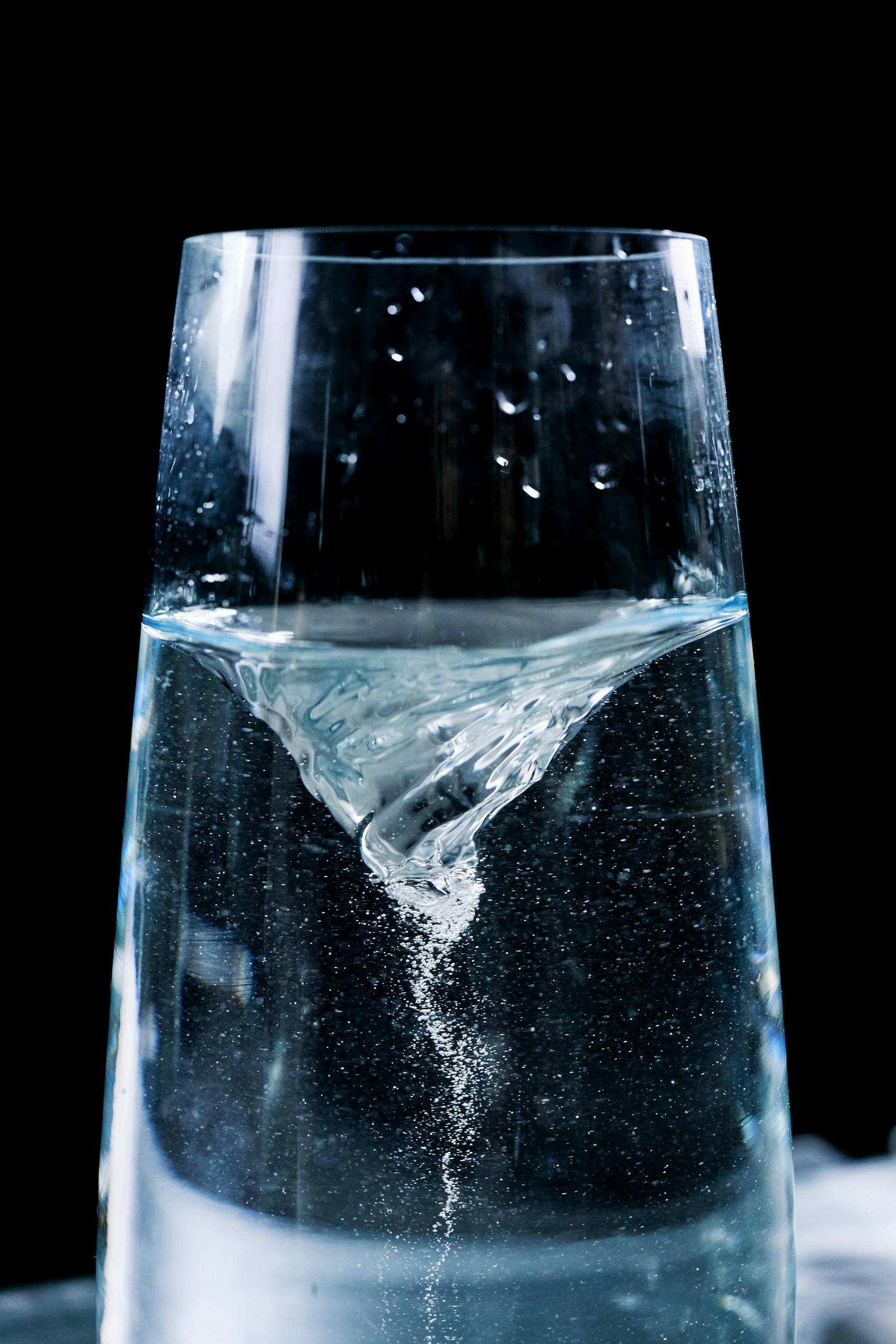 Close-up of a mesmerizing water vortex in a glass with droplets against a dark background.