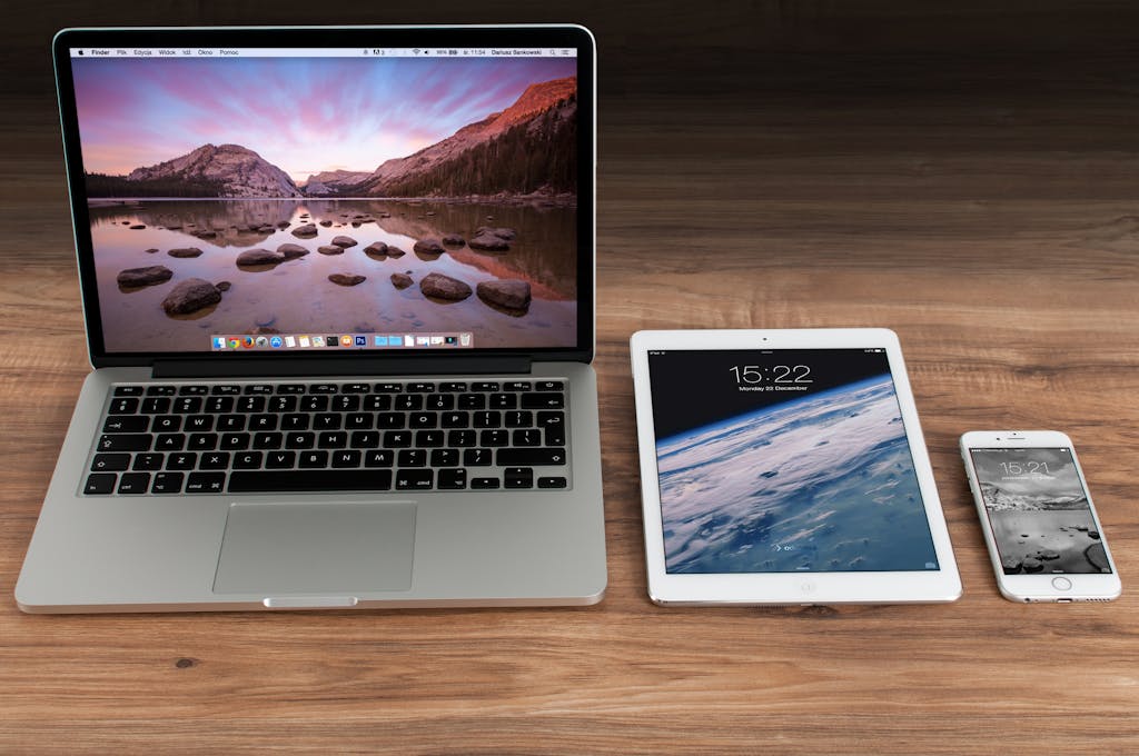 Modern workspace showcasing Apple laptop, tablet, and smartphone on a wooden desk.