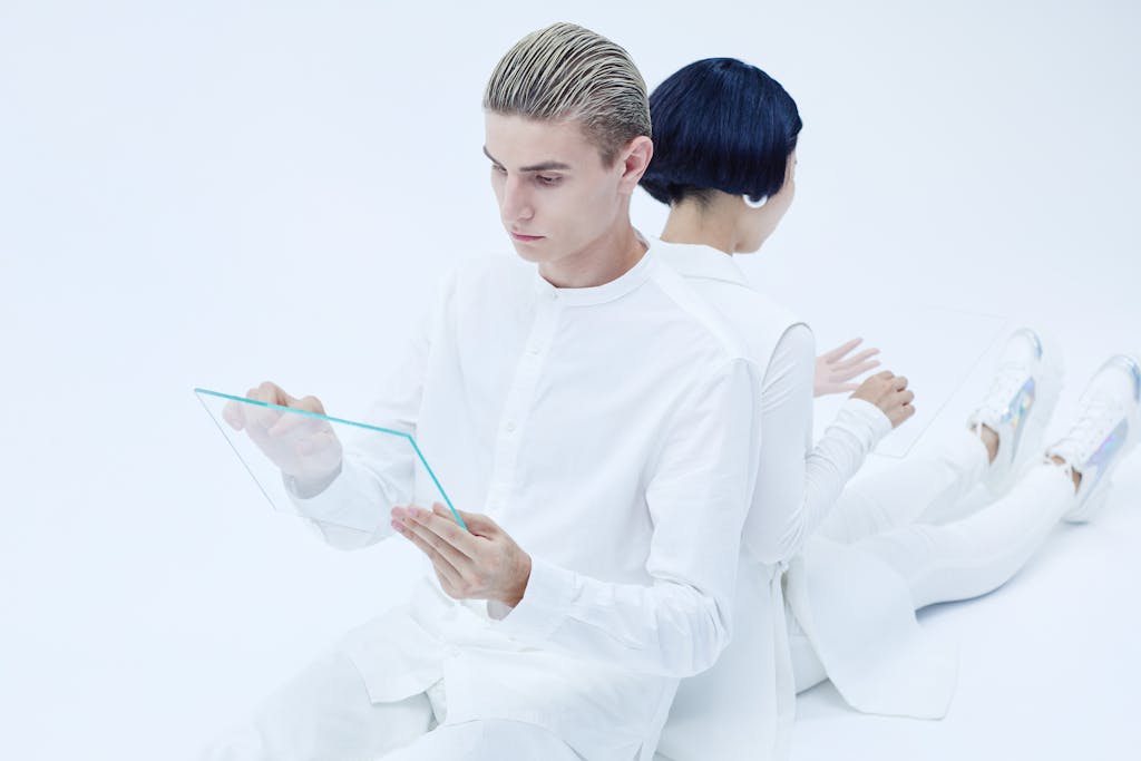 Two adults interacting with transparent tablets, showcasing modern technology in a futuristic white setting.