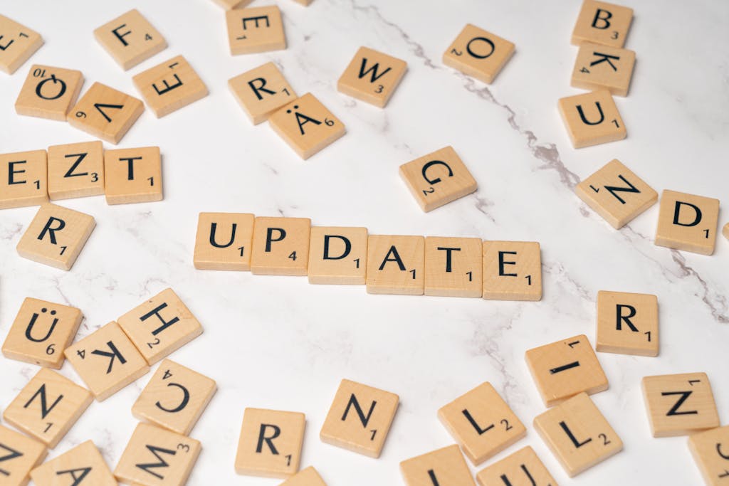 Wooden Scrabble tiles arranged to spell 'Update' among scattered letters on a marble background.