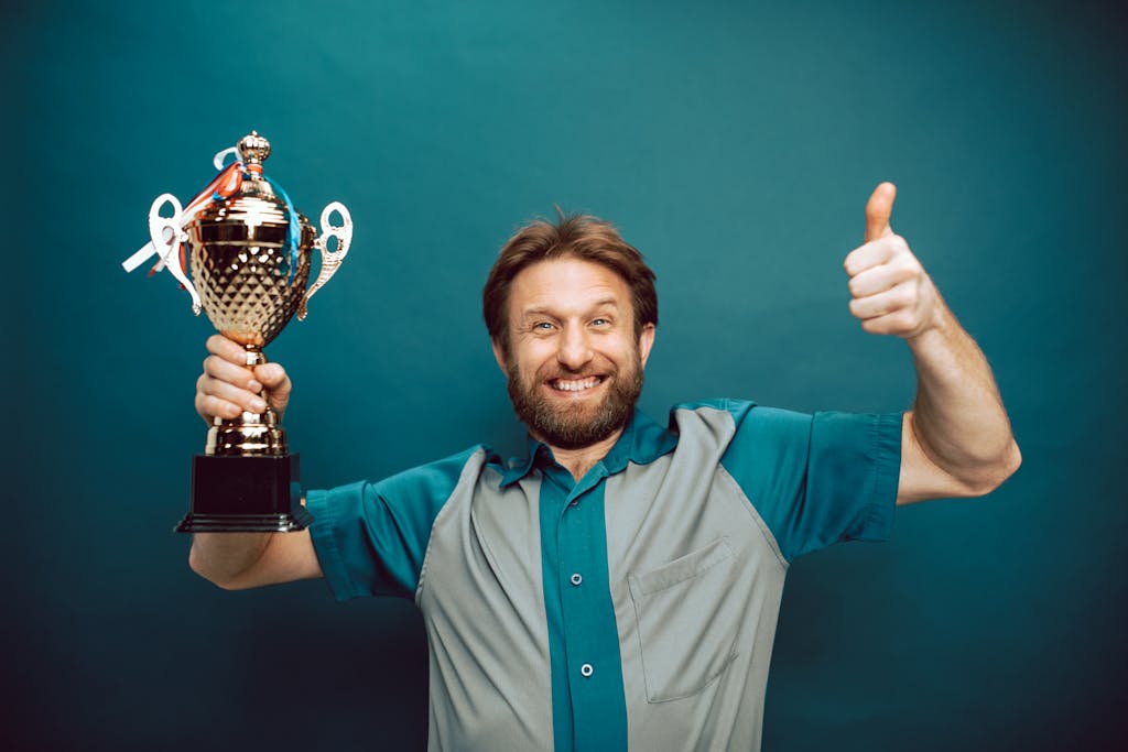 Smiling man holding a trophy and giving a thumbs up gesture against a blue backdrop.