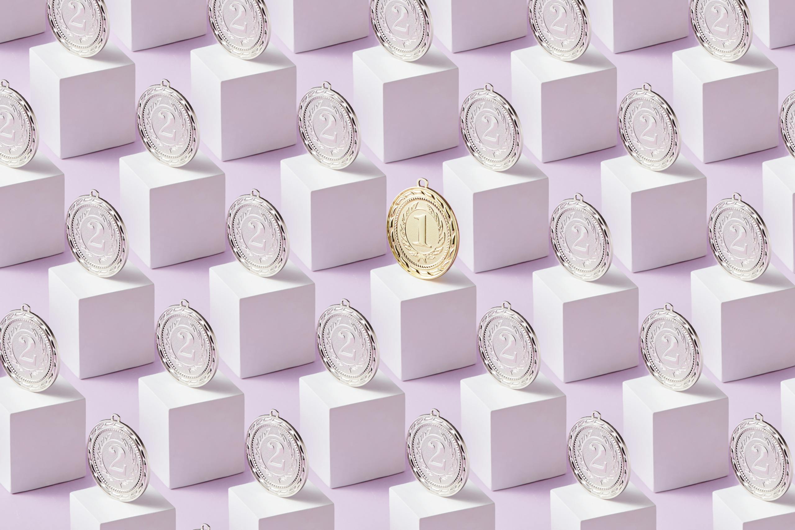 A gold medal stands out among silver medals on white cubes, showcasing uniqueness.